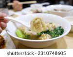 Woman’s hand holding a wonton on a soup spoon over a bowl of wonton noodle soup — at a Cantonese restaurant in Eastwood, Sydney; New South Wales, Australia