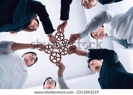 Hand holding wooden gear by businesspeople wearing suit for harmony synergy in office workplace. Bottom view office worker hand make chain of gear into collective unity form.