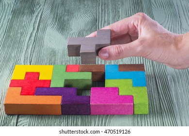 Hand holding wooden puzzle element. Hand sets the last element of the puzzle. The concept of logical thinking. Geometric shapes on a wooden background. Tetris toy wooden blocks.