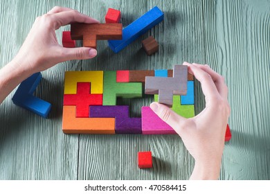 Hand holding wooden puzzle element. Hand sets the last element of the puzzle. The concept of logical thinking. Geometric shapes on a wooden background. Tetris toy wooden blocks.
