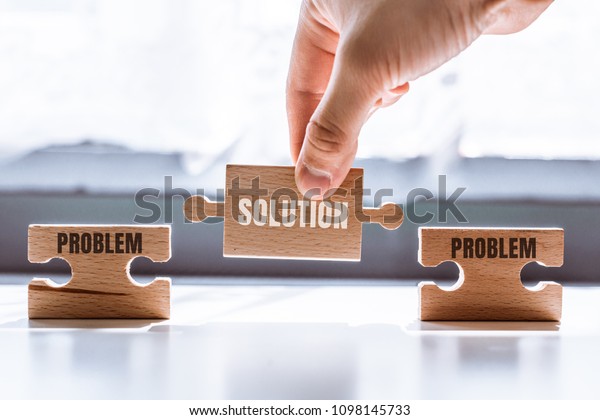 Hand holding a\
wooden puzzle with the word solution. There is a matching puzzle\
next to it with the word problem. The concept of solving problems,\
all problems can be\
solved.