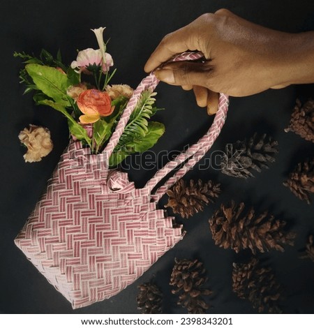 A hand holding a woven hand bag with flowers beside pine cones.  New years background
