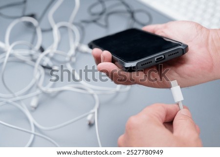 Hand holding a wrong type of electric charging cables before charging the phone battery, with confused usb wires on the table