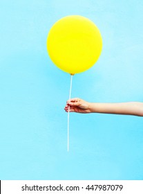 Hand holding yellow air balloon over colorful blue background