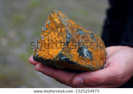 Hand holding a yellow and brown ore stone containing copper and other minerals, selective focus