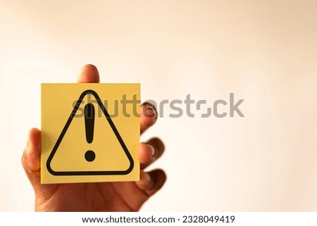 Hand holding yellow page with Exclamation mark or Warning sign over white background with copyspace concept for attention symbol,Cautionary Warning,safety, hazard,,caution, danger.