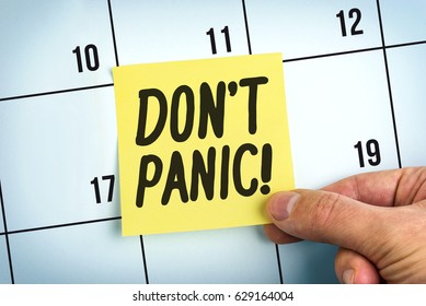 Hand Holding Yellow Paper Note With Words Don't Panic On Calendar