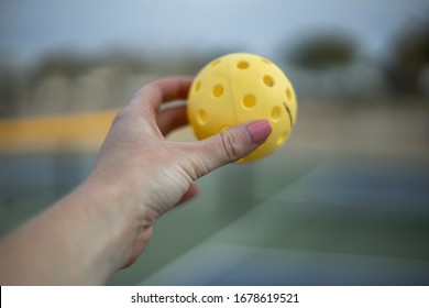 A Hand Holding A Yellow Pickleball Ball