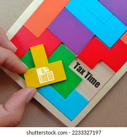 Hand holding yellow puzzle and text TAX TIME at space of wooden puzzle isolated brown background  - Shutterstock ID 2233327197