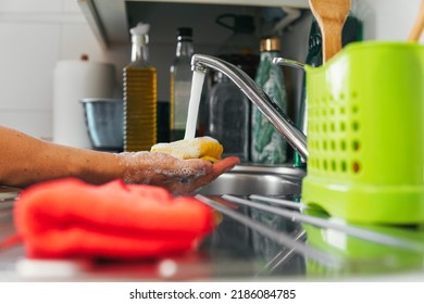 Hand holding yellow scouring pad with palm as water falls from faucet. Side shot of a dishwashing utensil making soap and foam. Concept of cleanliness