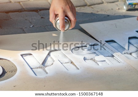 Hand holds an aerosol spray can, puts the image on the asphalt through a stencil