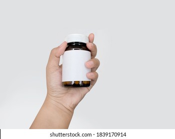 Hand  holds an amber glass vitamins, supplements and minerals dual layer tablets pills and medicine bottle to show or see the label on white background. There is copy space on the label. Blank label.