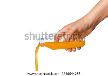 The hand holds a bottle of orange juice. Juice is pouring from a bottle. Isolated on white background.