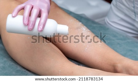 The hand holds the bottle and pours talcum powder on the client's feet before depilation. Selective focus.