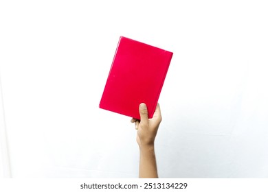 A hand holds a bright red book, against a plain white background. The book has a simple cover with a single uniform color.