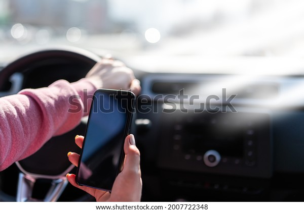 Hand holds the cell phone against the background of the\
steering wheel of the car. Distracted Driver With A Cell Phone.\
Phone with a blank black screen for an inscription or picture.\
Accident hazard 