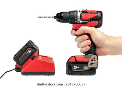 A hand holds a cordless drill on a white isolated background, side view. A set of a cordless drill and a charger that charges the battery from a screwdriver. - Powered by Shutterstock