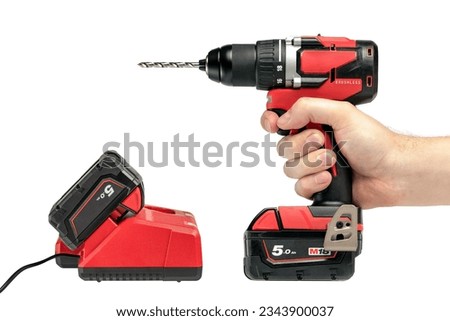 A hand holds a cordless drill on a white isolated background, side view. A set of a cordless drill and a charger that charges the battery from a screwdriver.