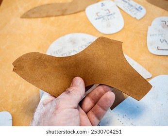 A hand holds a cut leather pattern piece used for footwear design, part of the shoemaking process, illustrating precision and craftsmanship in shoe production - Powered by Shutterstock