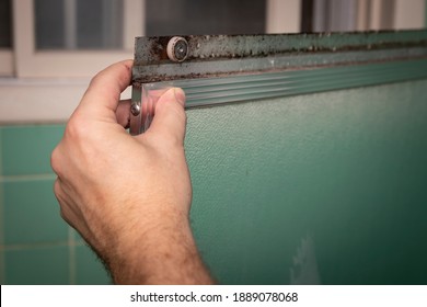 Hand Holds Dirty Sliding Shower Door Frame, In Retro Colored And Styled Home Bathroom Setting.