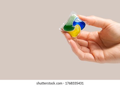 hand holds the Dishwasher Capsule on beige background. copy space. woman hand holding dishwasher detergent tablet.