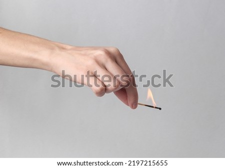 Hand holds a dying match on a gray background