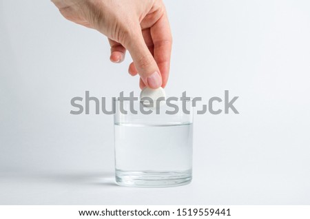 A hand holds an effervescent soluble tablet and places it in a glass of water. Isolated on white background. The concept of treatment and prevention of viral diseases. Help for depression and insomnia