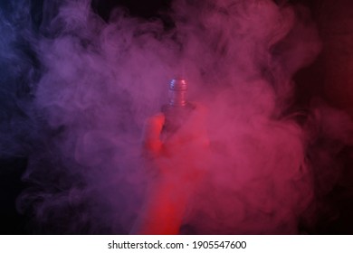 Hand holds an electronic cigarette or vaping device in dense smoke with pink blue neon light.