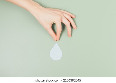 Hand Holds Falling Drop On Green Background. World Water Day, Shortage Of Drinking Water, Save Water Concept