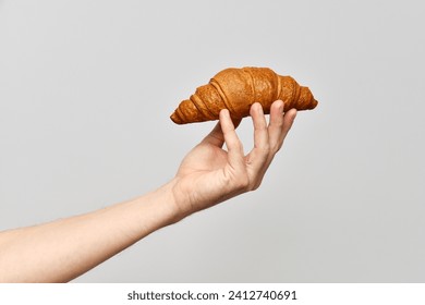 Hand holds a fresh, crispy croissant. French traditional food. Delicious European baked goods. Hold food, empty background, copy space. - Powered by Shutterstock