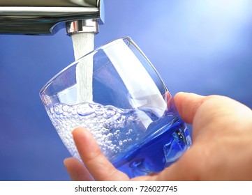 A Hand Holds A Glass Under A Stream Of Clear Transparent Cold Water From A Tap On A Blue Background Close-up Of A Macro.