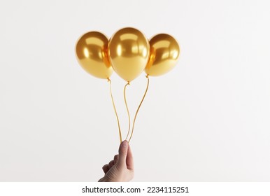 Hand holds gold balloons on a light background. Concept for the release of balloons, balloons inflated with air.