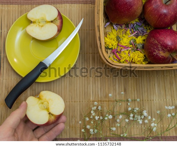 Hand holds half of apple near plate with knife and\
second part