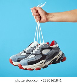 Hand holds hanging colored running sneakers by the laces on blue pastel background. Hand with a new casual shoe. Close up. - Powered by Shutterstock