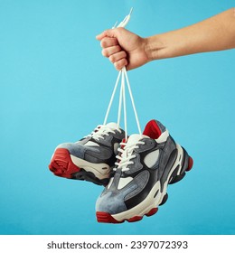 Hand holds hanging colored running sneakers by the laces on blue pastel background. Hand with a new casual shoe. Close up. - Powered by Shutterstock