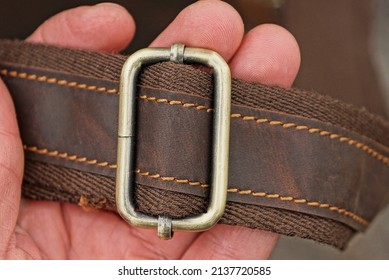 a hand holds the harness of a bag made of leather and fabric with a gray metal buckle