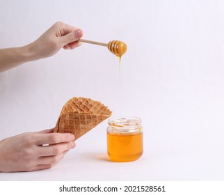 Hand Holds Honey Spoon With Jar Of Bee Honey And Waffle Cone On White Background