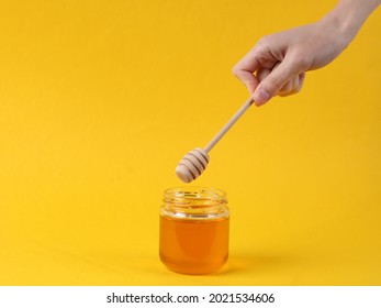 Hand Holds Honey Spoon With Jar Of Bee Honey On Yellow Background