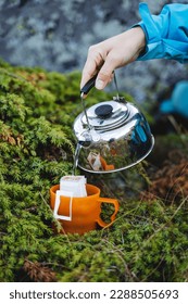 The hand holds the kettle in nature to pour boiling water into a mug, brew a coffee filter bag, an instant drink in nature, a quick preparation of breakfast. High quality photo