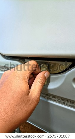 A hand holds a latch to open a folding table on a passenger seat in an airplane cabin