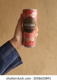 Hand holds limited edition Nescafe Ros Bandung. Tanned skin. Unique blend of rose floral notes, creamy milk and coffee. Canned drink. Brown wall textured background. Malaysia. October 2021