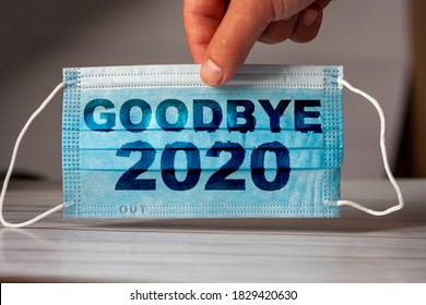 The hand holds a medical and protective mask with the word GOODBYE 2020. Concept of coronavirus quarantine. Prevent or stop the spread of the COVID-19 worldwide.