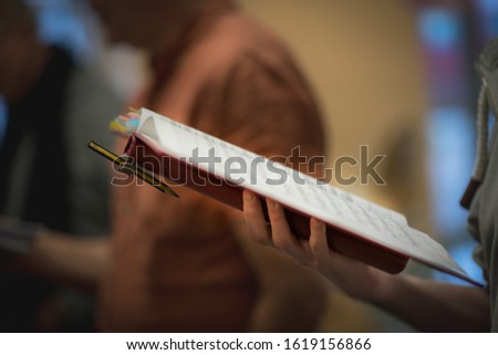 Hand holds notes during choir rehearsal, shallow depth of field