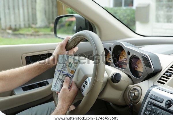 hand holds one hundred dollar bills in cash against\
the background of a steering wheel of a car. Concept of sale,\
purchase and leasing of\
cars.