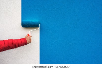 hand holds paint roller and painting a wall
