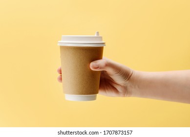 Hand Holds A Paper Can For Coffee Or Tea On A Yellow Background With Place For Text. Coffee To Go Concept.