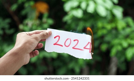 A hand holds a piece of paper with the number "2024" slowly burning. Concept for the end of 2024 - Powered by Shutterstock