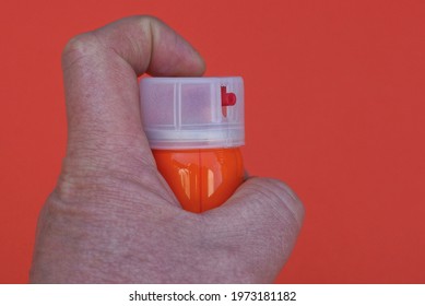 Hand Holds A Pink Metal Gas Bar With A White Plastic Cap On A Red Background