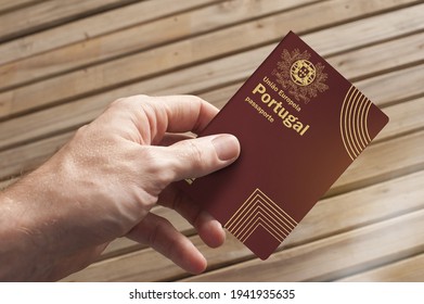 A hand holds a Portuguese passport and a wooden board in the background, copy space