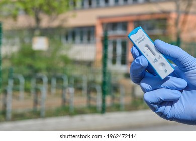 Hand Holds Quick Test Outdoors, With Office, School Or Kindergarden Building Out Of Focus. Express COVID19 Test, Schnelltest Is Rapid Corona Test In German. Selbsttest Means Coronavirus Self-test.